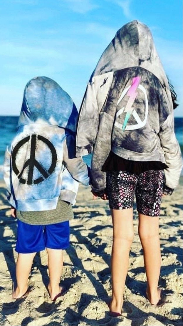Two children at the beach wearing peace sign graphic hoodies.
