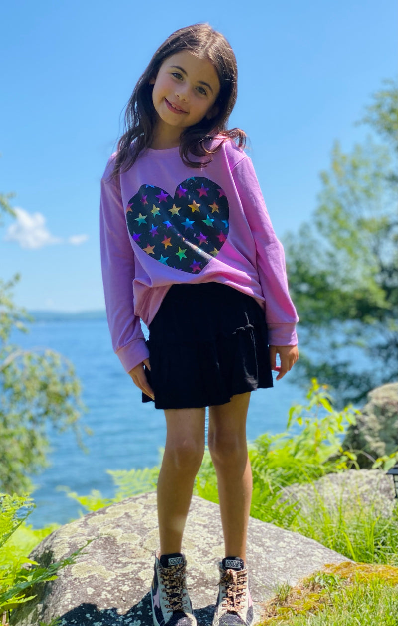 Young girl wearing a pink sweatshirt with a colorful heart on it.